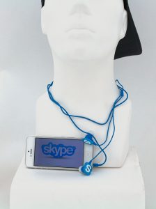 Bild mit Iphone auf dem ein Skype-Logo zu sehen ist, sowie Kopfhörer mit Sykpe-S um einem Kunststoff-Kopf
